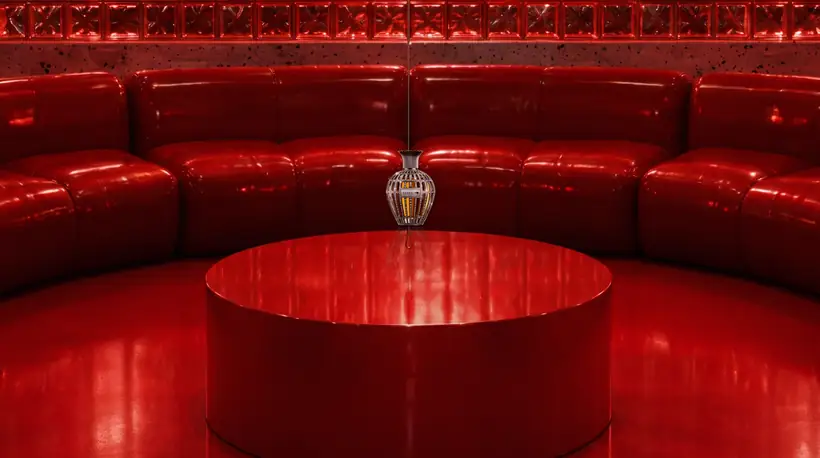 A crystal-caged perfume flacon of amber glass hanging on a thin chain above the round table in the red pit