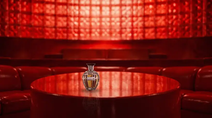 The flacon standing on the round red plinth, a curved wall of glowing red glass blocks behind it and red sofas in the foreground
